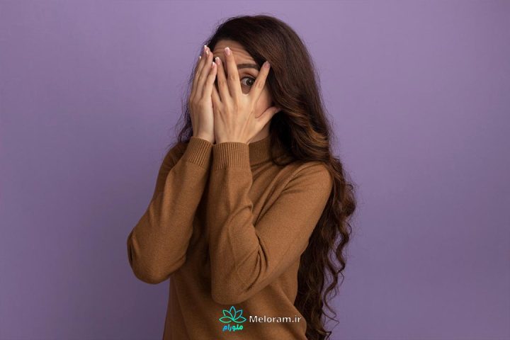 زنی با لباس قهوه ای که از ترس چشم های خود را بسته و با یک چشم در حال نگاه کردن است.