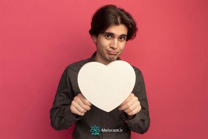 مردی با لباس قهوه ای و پس زمینه قرمز با یک قلب سفید در دست