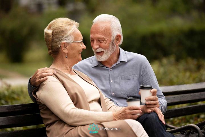 یک زوج مسن خوشحال که در پارک نشسته اند و در حال صحبت و لبخند زدن به یکدیگر هستند.