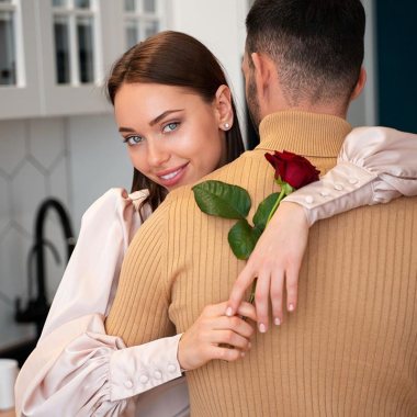 زنی که با یک گل رز در دست همسر خود را در آغوش گرفته است.